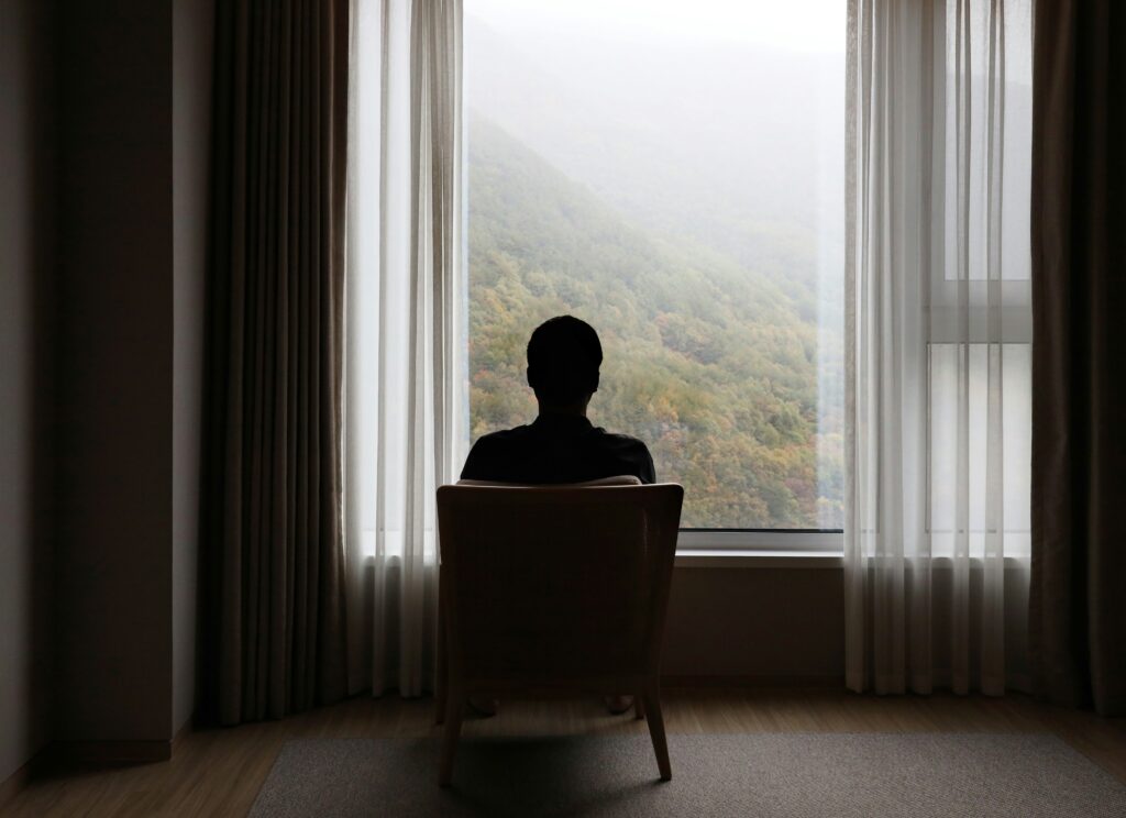 Grief That Doesn't Look Like Sadness: What Grief Actually Feels Like Adult sitting quietly alone near a window, the private, inward experience of grief that doesn't always look like sadness.
